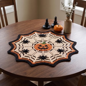 May include: A round, crocheted table doily featuring a cream-colored spiderweb pattern, a central orange jack-o'-lantern, and several small black spiders attached to the web. The border is trimmed in alternating bands of orange and black yarn.