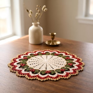 May include: A round, crocheted doily featuring a central cream-colored circular pattern surrounded by a ring of dark green leaves and small red berries, finished with a scalloped border in red and cream with a thin gold-colored metallic trim.
