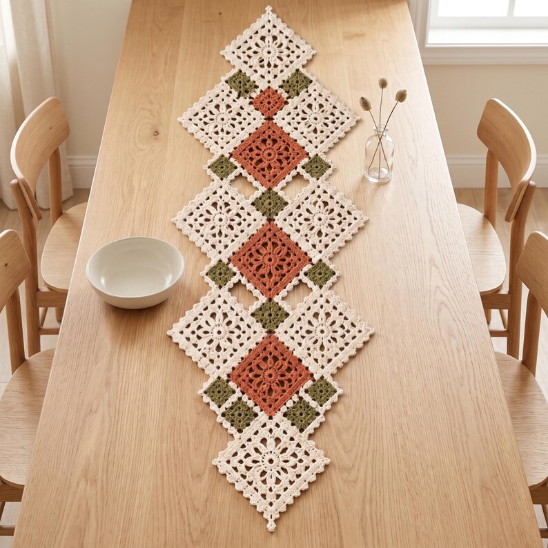May include: A long, diamond-shaped crochet table runner featuring a repeating pattern of cream, terracotta, and olive green squares. The intricate, openwork floral design is constructed from joined motifs, creating a geometric, lace-like texture.