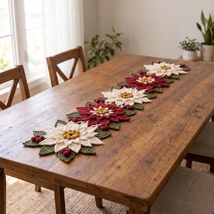 May include: A long, crocheted table runner featuring a repeating pattern of poinsettia flowers in cream and deep red, accented with dark green leaves and small red berries. The floral motifs are arranged in a line along the center of the table.