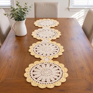May include: A long table runner composed of four connected circular crochet doilies. Each doily features an intricate cream-colored center with a floral-like pattern, bordered by a scalloped edge in a soft, pale yellow yarn color.