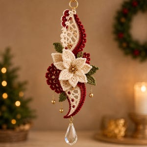 May include: A decorative hanging ornament featuring a central cream-colored crocheted poinsettia flower with a gold bead center, surrounded by dark red and green crocheted leaves and lace accents, finished with a clear teardrop crystal pendant.