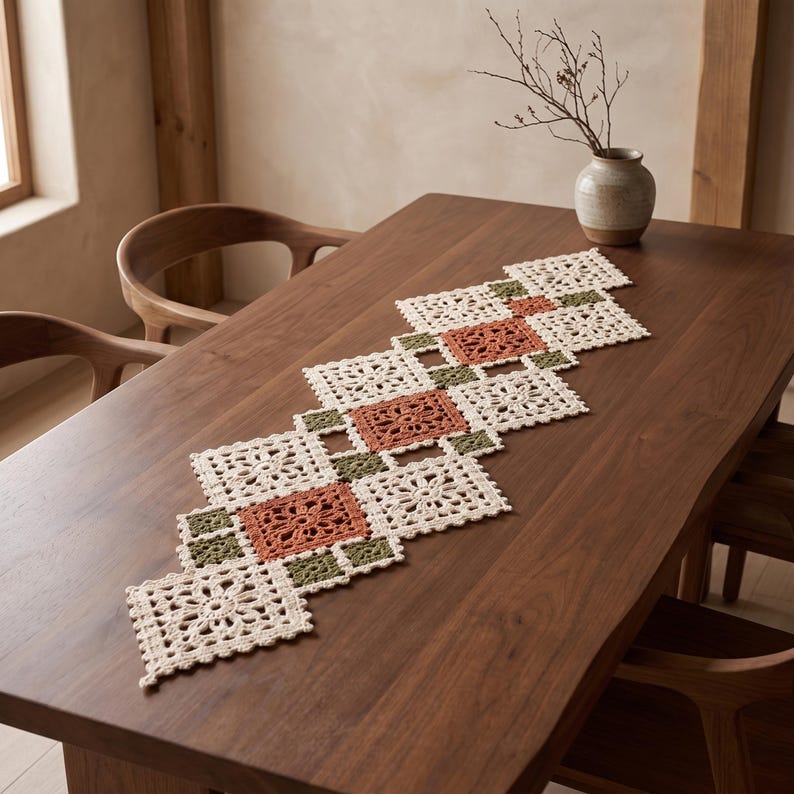 May include: A rectangular crochet table runner featuring a geometric pattern of interconnected squares in cream, terracotta, and olive green. The design consists of large floral-motif squares joined by smaller solid squares, creating a lace-like texture.