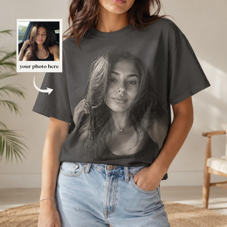 May include: A charcoal gray short-sleeve t-shirt featuring a large, centered black and white photographic print of a person. A small inset box in the upper left corner displays a photo of the same person with the text your photo here.