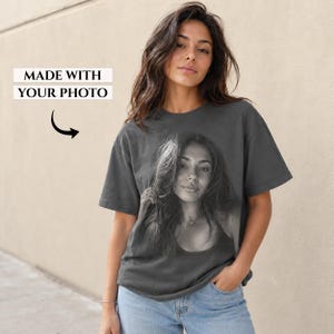 May include: A charcoal gray short-sleeve t-shirt featuring a large black and white photographic print of a person on the front. Above the print, the text reads MADE WITH YOUR PHOTO with a black arrow pointing down toward the image.