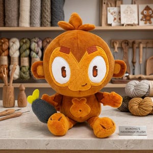 May include: A plush monkey toy with golden-brown fur, large white eyes, and a small smile. It features a tuft of hair on its head and holds a dark grey, textured object with a bright yellow tip. A small silver sign reads WUKONG'S HANDMADE PLUSH.