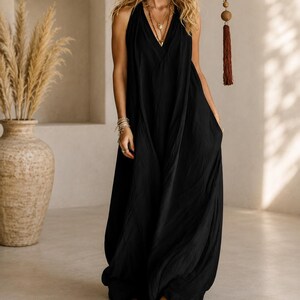 May include: A floor-length black sleeveless dress with a deep V-neckline and a loose, flowing silhouette. The garment features a gathered bodice and a long, draped skirt that reaches the floor, creating a relaxed and comfortable fit for the wearer.