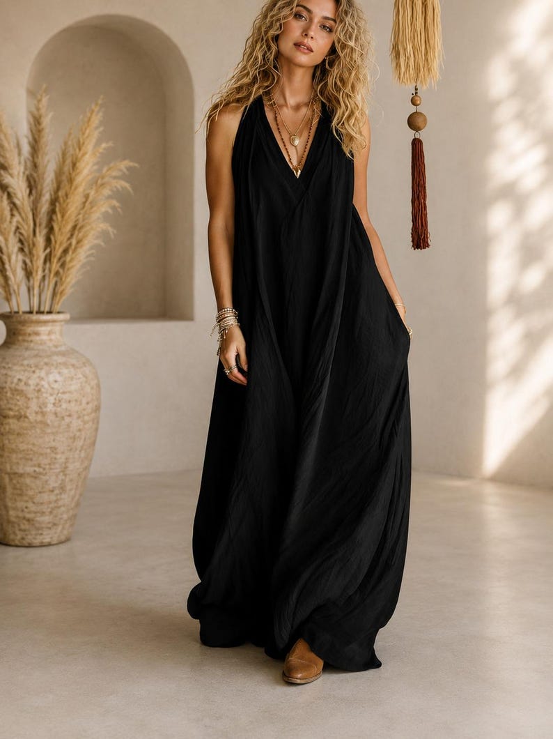 May include: A floor-length black sleeveless dress with a deep V-neckline and a loose, flowing silhouette. The garment features a gathered bodice and a long, draped skirt that reaches the floor, creating a relaxed and comfortable fit for the wearer.