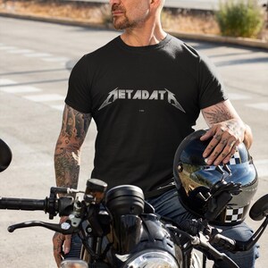 May include: A black short-sleeved t-shirt featuring the word METADATA printed in a metallic silver, stylized font across the chest. The shirt has a crew neckline and a standard fit, constructed from a solid black fabric with a clean, simple design.