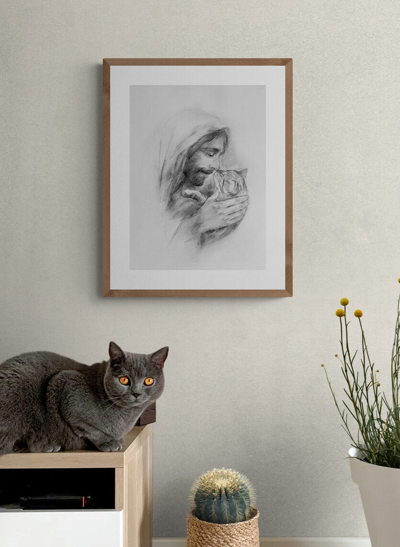 May include: A framed black and white pencil drawing of a man holding a small animal. The man has a beard and long hair. The drawing is on a white background and is framed in a light brown wood frame. A gray cat is sitting on a wooden shelf in the foreground.