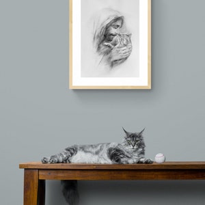 May include: A black and white drawing of a man holding a cat in his arms. The drawing is framed in a light wood frame and is hanging on a light blue wall. A gray cat is lying on a wooden bench with a white baseball in front of it.
