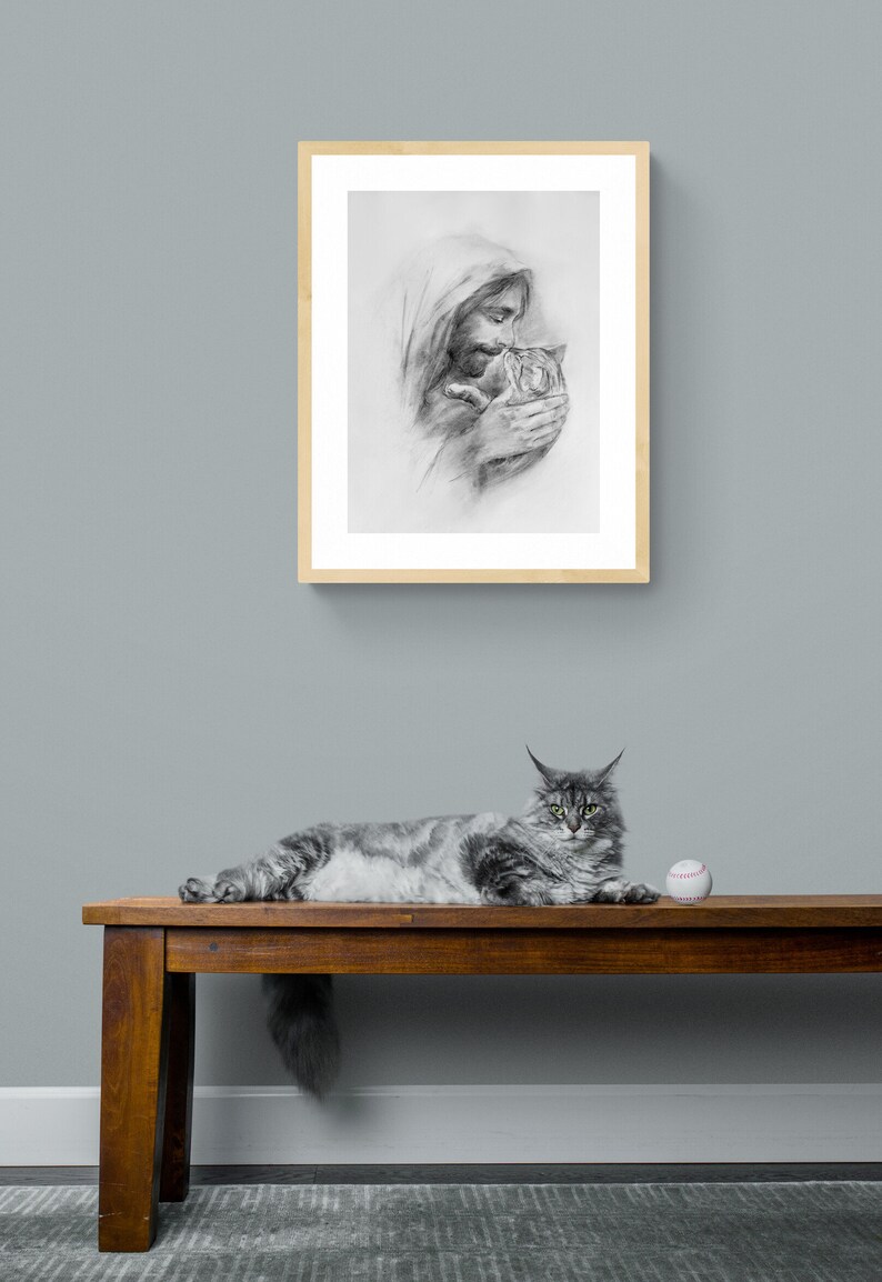 May include: A black and white drawing of a man holding a cat in his arms. The drawing is framed in a light wood frame and is hanging on a light blue wall. A gray cat is lying on a wooden bench with a white baseball in front of it.