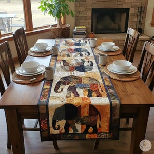 Pode incluir: Um caminho de mesa retangular de tecido com um design de patchwork de elefantes estilizados em tons de laranja, castanho, azul e creme. O caminho est&aacute; centrado numa mesa de jantar de madeira com ta&ccedil;as brancas, canecas e individuais.