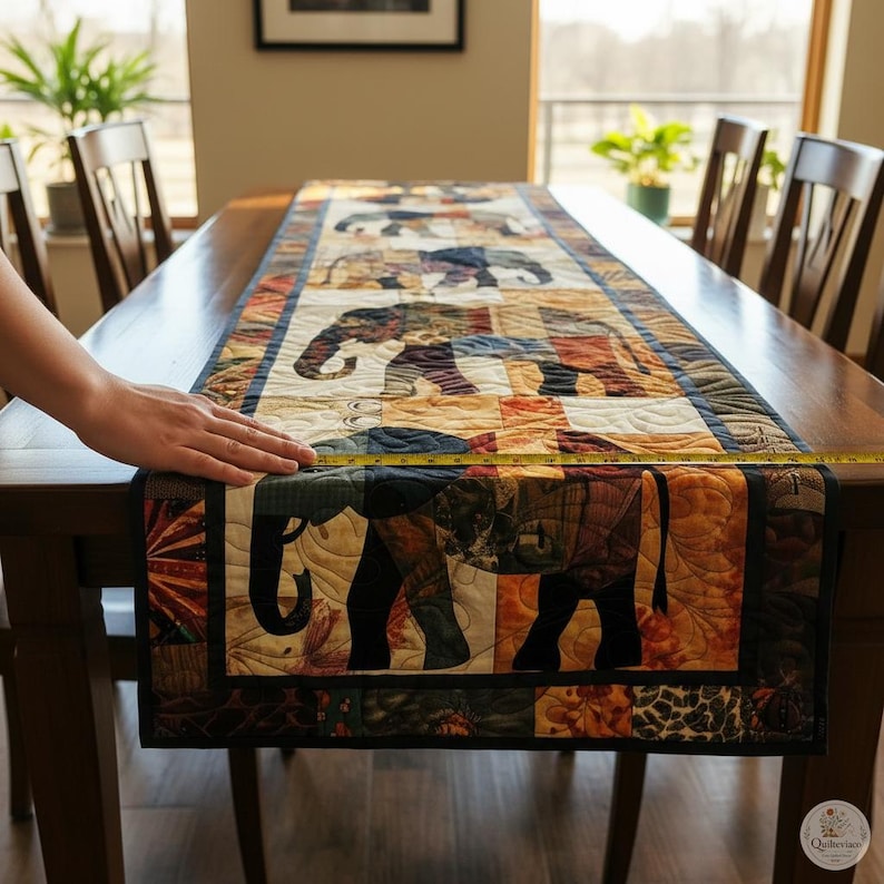 Pode incluir: Um caminho de mesa retangular de tecido com um padr&atilde;o de patchwork repetitivo de elefantes em tons de castanho, azul e laranja. Uma fita m&eacute;trica amarela est&aacute; colocada na largura, mostrando uma medida de aproximadamente 35,5 cm.