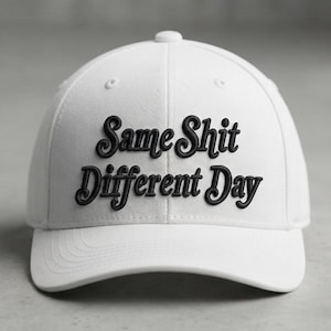 Può includere: Un cappellino da baseball bianco con il testo Same Shit Different Day ricamato in filo nero sulla parte anteriore. Il cappellino presenta una corona strutturata, una visiera curva e un bottone sulla parte superiore, con caratteri corsivi.