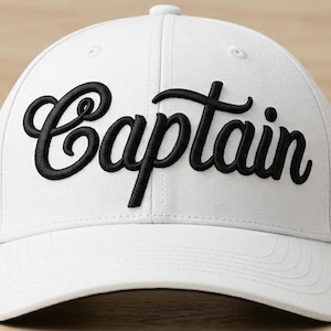 Puede incluir: Una gorra de béisbol blanca con la palabra Captain bordada en letras cursivas negras en la parte delantera. La gorra tiene una corona estructurada, una visera curva y un botón superior, mostrando un diseño limpio con costuras negras.