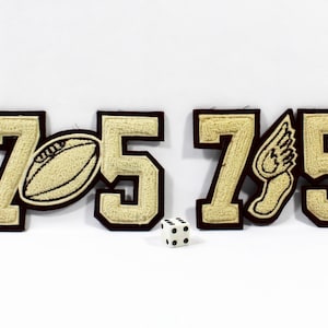 May include: A collection of embroidered patches featuring the number 75 in a varsity style. One patch includes a football, another a winged foot. A small, white die with black dots is also present.