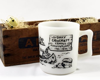 May include: White ceramic mug with a black and white illustration of Davy Crockett in a canoe. The text on the mug reads "Davy Crockett Famous Frontiersman 1786-1836".