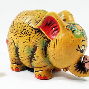 May include: A yellow ceramic elephant piggy bank with red ears, green and blue floral accents, and a pink piglet on its trunk.