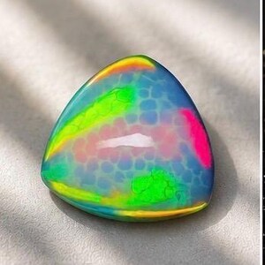May include: A triangular cabochon gemstone featuring a translucent blue base with a honeycomb-like pattern. The surface displays vibrant, iridescent flashes of neon green, bright pink, and yellow, creating a multi-colored play of light.