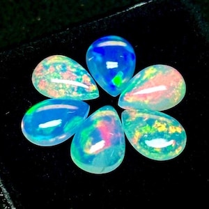 Può includere: Sei opali a forma di pera disposti in un motivo circolare. Ogni gemma mostra un corpo traslucido con lampi iridescenti di luce blu, verde, rosa e gialla. Le pietre hanno una superficie liscia e lucida e una silhouette a forma di goccia.