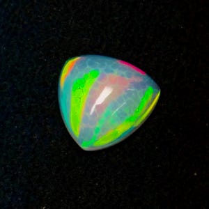 May include: A triangular-shaped opal gemstone featuring a translucent, milky white base with a honeycomb pattern. The surface displays vibrant flashes of neon green, bright pink, and yellow light, creating a multi-colored play of color effect.