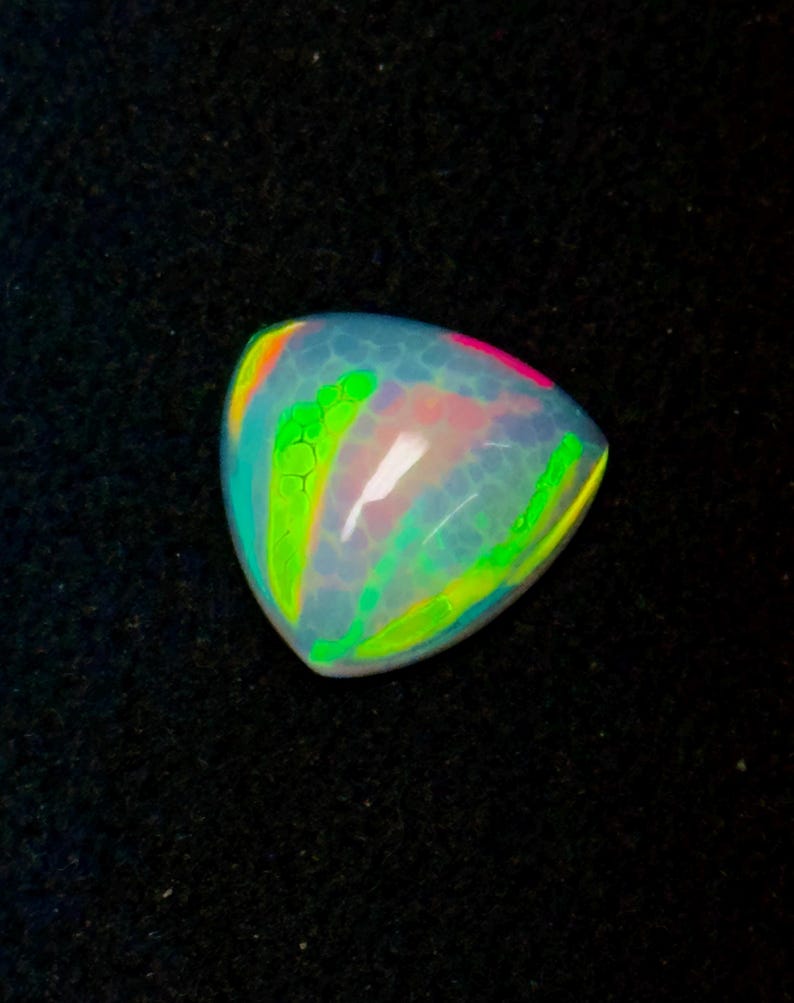 May include: A triangular-shaped opal gemstone featuring a translucent, milky white base with a honeycomb pattern. The surface displays vibrant flashes of neon green, bright pink, and yellow light, creating a multi-colored play of color effect.