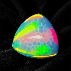 May include: A triangular cabochon gemstone featuring a translucent, milky white base with a distinct honeycomb pattern. The surface displays vibrant, iridescent flashes of neon green, bright yellow, and hot pink across its smooth, domed top.