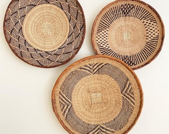 Könnte beinhalten: Drei runde geflochtene Körbe mit komplexen geometrischen Mustern aus naturfarbenen und dunkelbraunen Fasern. Jeder Korb hat ein eigenes Design mit einem zentralen geflochtenen Quadrat und einem dicken, verstärkten Rand.