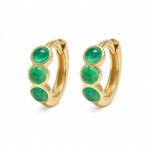 May include: A pair of gold hoop earrings, each featuring three round, cabochon-cut green gemstones set vertically along the front of the hoop. The metal has a polished, reflective finish, and the design includes a hinged closure mechanism.