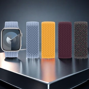 Może przedstawiać: Srebrny smartwatch z jasnoniebieskim plecionym paskiem typu solo loop, prezentowany obok czterech dodatkowych plecionych pasków w kolorach jasnoniebieskim, żółtym, ciemnobordowym oraz czarnym wielokolorowym splocie, wszystkie o teksturze.