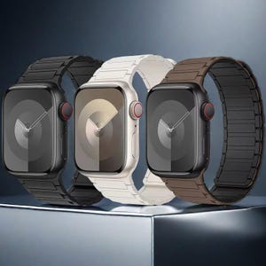 Op de afbeelding: Drie smartwatches met rechthoekige schermen en schakelbanden in zwart, wit en bruin. Elke horloge heeft een digitale wijzerplaat met dunne wijzers en een ronde kroon aan de zijkant. De apparaten staan naast elkaar in een rij opgesteld.