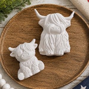 May include: Two white, unpainted Highland cow figurines with textured fur and curved horns. The larger figurine stands upright, while the smaller one is in a seated position. Both figures are crafted from a solid, matte material.
