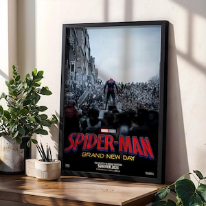 May include: A framed movie poster for Spider-Man Brand New Day featuring a figure in a red and blue suit standing before a large crowd in a city street. The text reads Marvel Studios, Spider-Man Brand New Day, and Exclusively in Movie Theaters Summer 2026.