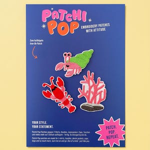 Op de afbeelding: Een blauwe displaykaart met drie geborduurde strijkpatches: een roze heremietkreeft met een groene schelp, een rode kreeft en een roze koraal. De kaart bevat de tekst Patchi Pop, Embroidery Patches With Attitude en Patch. Pop. Repeat.