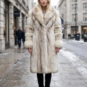 Peut inclure: Un long manteau en fourrure crème et brun clair avec un large col et des manches à revers. Le manteau présente un poil épais et texturé avec des motifs verticaux sur tout le vêtement, descendant jusqu'au mi-mollet, porté avec un pantalon noir.