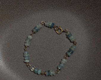 May include: A delicate bracelet featuring small, faceted, light blue aquamarine gemstone beads strung on a thin gold-toned metal wire. The piece is secured with a circular spring ring clasp, showcasing a simple design with alternating beads and gold links.