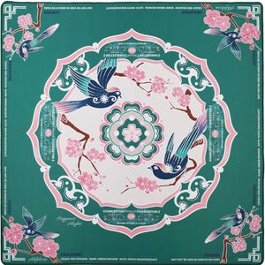 May include: A square teal Mahjong mat featuring a central white circular mandala with pink cherry blossoms and two blue birds. The border displays text including "Dragons," "Jokers," and "Charleston" instructions, with corner illustrations of birds on flowering branches.