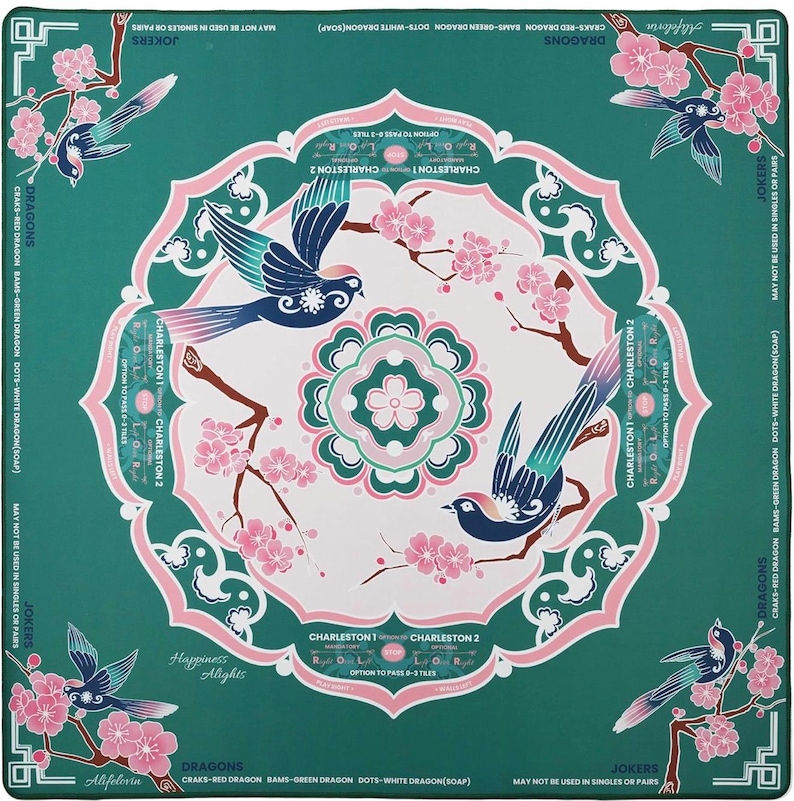 May include: A square teal Mahjong mat featuring a central white circular mandala with pink cherry blossoms and two blue birds. The border displays text including "Dragons," "Jokers," and "Charleston" instructions, with corner illustrations of birds on flowering branches.