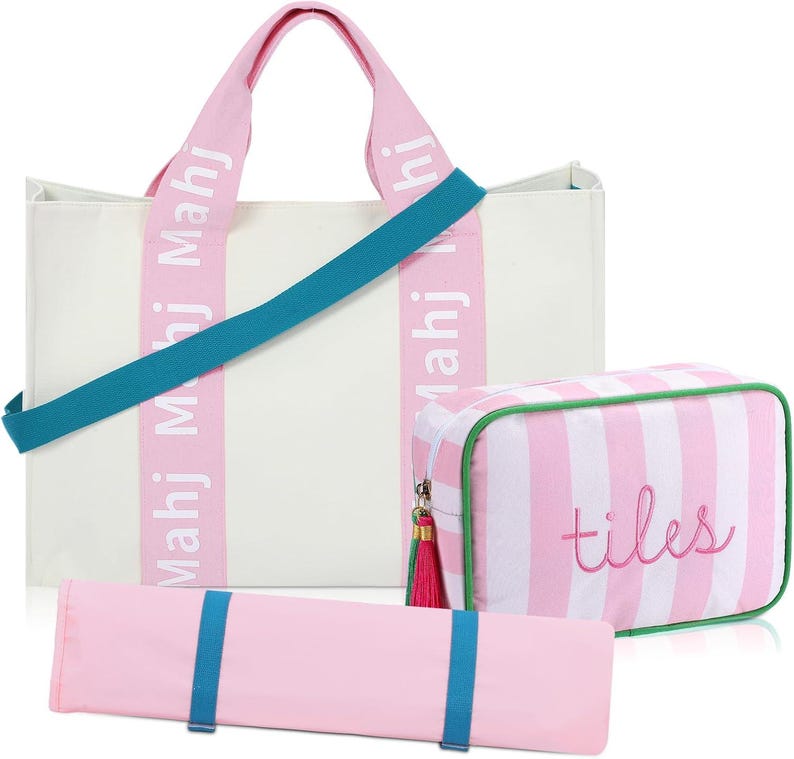 May include: A white canvas tote bag with pink straps featuring the text Mahj Mahj, a teal shoulder strap, a pink and white striped rectangular pouch with the word tiles embroidered in pink, and a long pink roll with two teal elastic bands.