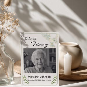 May include: A rectangular memorial card featuring the text In Loving Memory, a black and white photograph of an elderly person, the name Margaret Johnson, and the dates November 19, 1945 - June 2, 2026, decorated with a watercolour dove and green leaves.