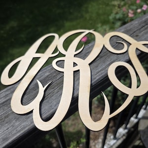 May include: A light-colored wooden monogram cutout featuring the interconnected, cursive-style letters A, R, and S. The piece is crafted from a flat, smooth material with a natural wood grain finish, showcasing elegant, flowing lines and curves.