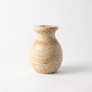 May include: A small, rounded vase crafted from beige travertine stone. The vessel features a natural, porous texture with horizontal, wavy bands of tan and cream colours throughout its surface, ending in a wide, flat-rimmed opening at the top.