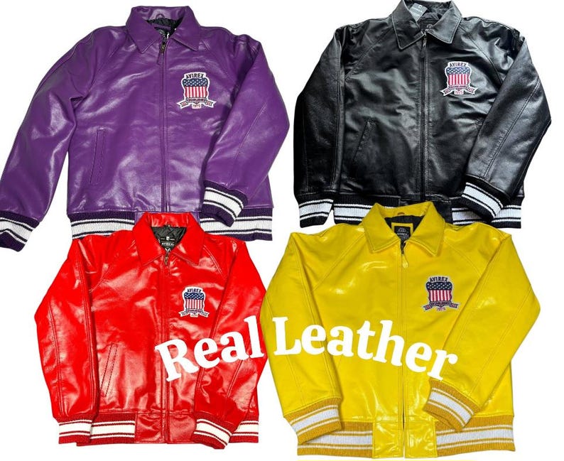May include: Four leather jackets in purple, black, red, and yellow. Each jacket features a front zipper, a collar, and a patch on the left chest displaying an American flag shield with the text "AVIREX". The text "Real Leather" is visible.