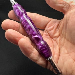 May include: A stylus featuring a contoured, pearlescent purple resin body with a swirling, marbled texture. The tool is capped with polished silver-toned metal tips at both ends, providing a sleek, ergonomic design for digital navigation.