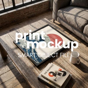 May include: A square black frame containing a print of a large blue ocean wave with white foam and a red sun against a cream background. The text print mockup SMART OBJECT FILE is overlaid on the image. A white mug and books are nearby.