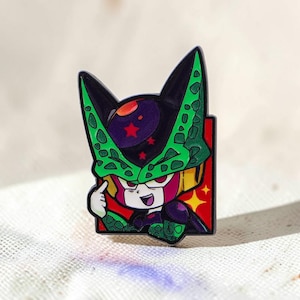 Peut inclure: Une broche en émail métallique représentant un personnage stylisé avec une tête tachetée de vert et de noir, un orbe frontal violet avec des étoiles rouges et un fond rouge avec des étoiles jaunes. Le personnage pointe sa tête du doigt.