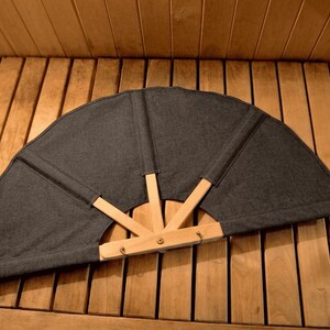 Peut inclure: Un grand éventail semi-circulaire doté d'une toile gris foncé fixée sur une structure en bois clair. L'éventail est composé de quatre baleines en bois qui s'étendent à partir d'un point de pivot central pour soutenir les sections en tissu.