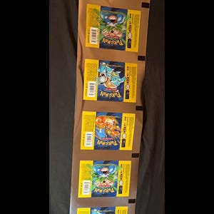 May include: A continuous vertical strip of metallic foil Pokémon trading card booster packs. The yellow and blue packaging features illustrations of Blastoise, Charizard, and Venusaur, with the Pokémon logo and text printed on each individual pack.