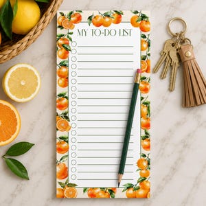 May include: A rectangular notepad with the text MY TO-DO LIST at the top, featuring a border of orange fruit and green leaves. The notepad has a column of circular checkboxes and horizontal lines, with a dark green pencil resting on the paper.